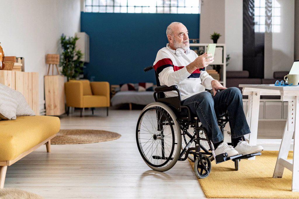 Thoughtful businessman with mobile phone on wheelchair at home