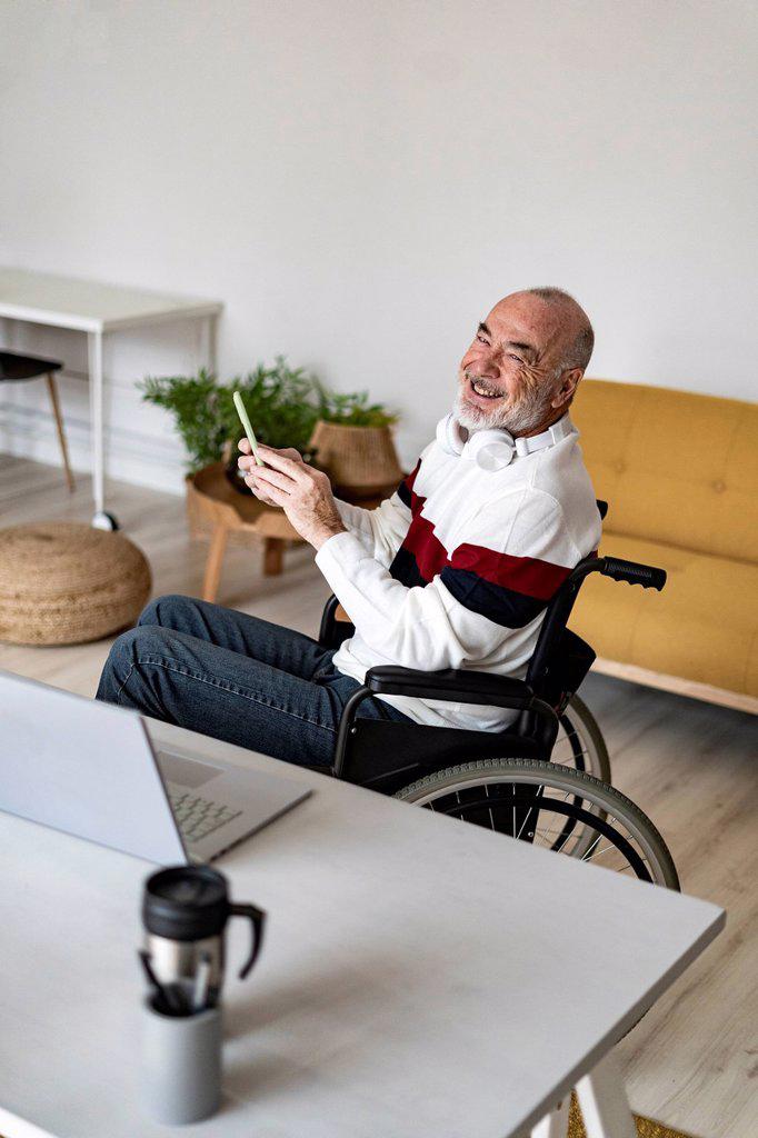 Smiling freelancer holding mobile phone on wheelchair at home office