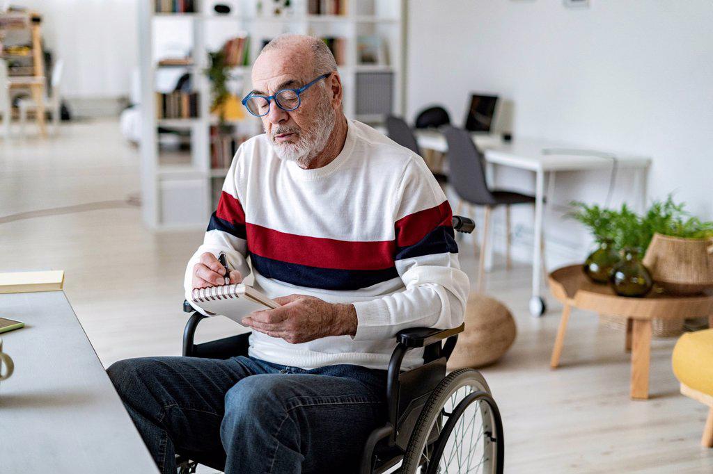Senior disabled businessman writing on notepad in living room