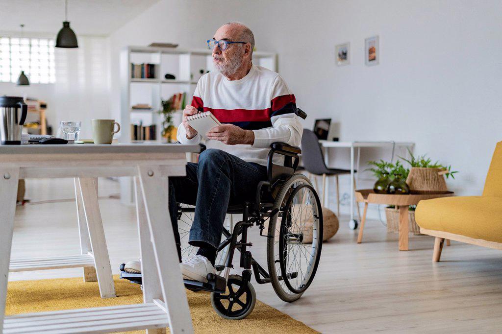Thoughtful businessman with note pad on wheelchair at home