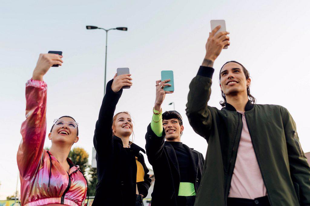 Smiling friends taking selfies through smart phones together