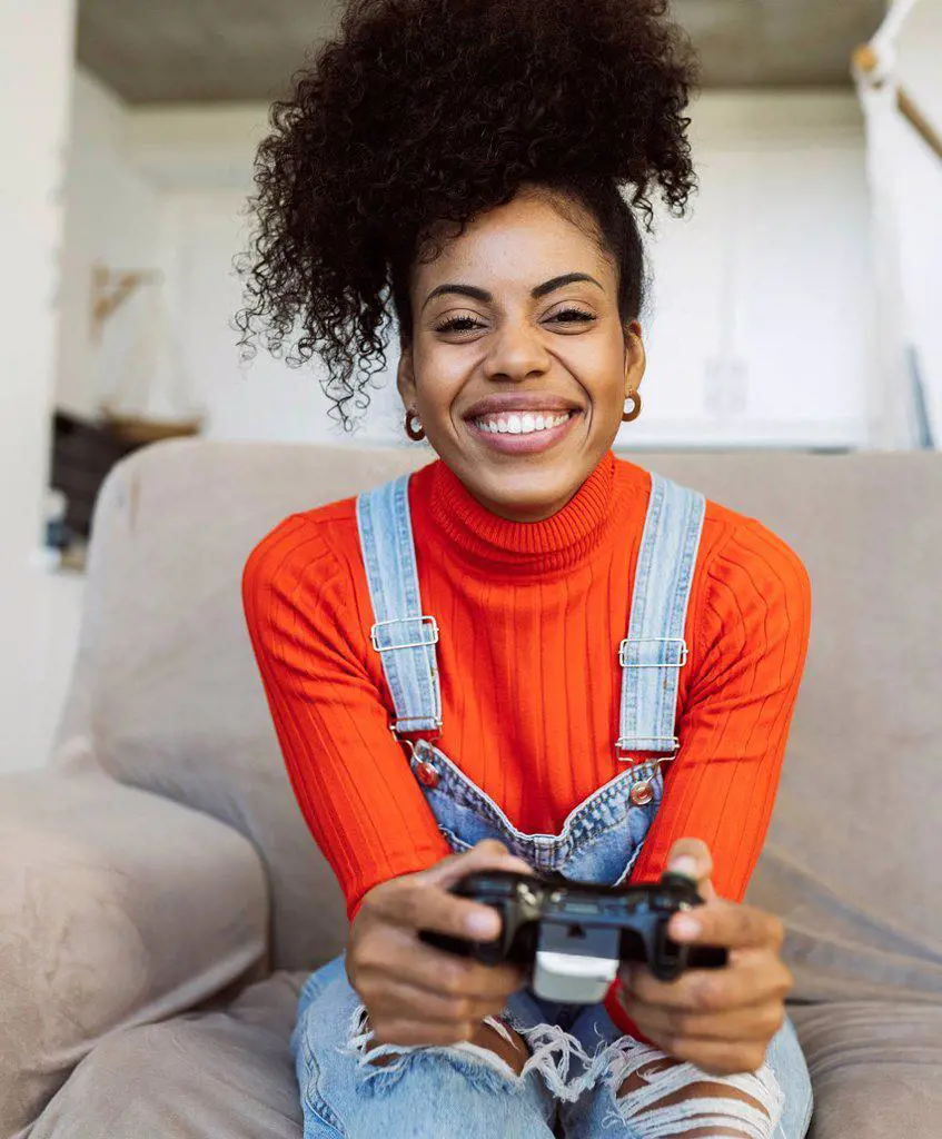 Happy curly haired woman playing video game on sofa