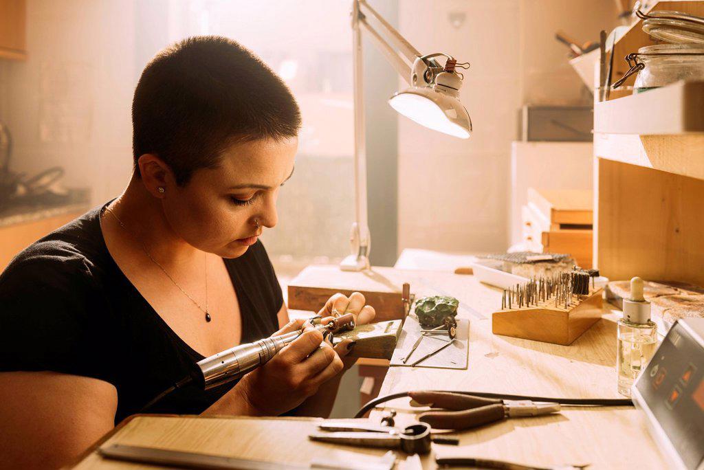 Female jeweler making silver ring using work tool in workshop