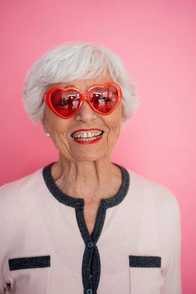 Happy woman with heart shape sunglasses against pink background