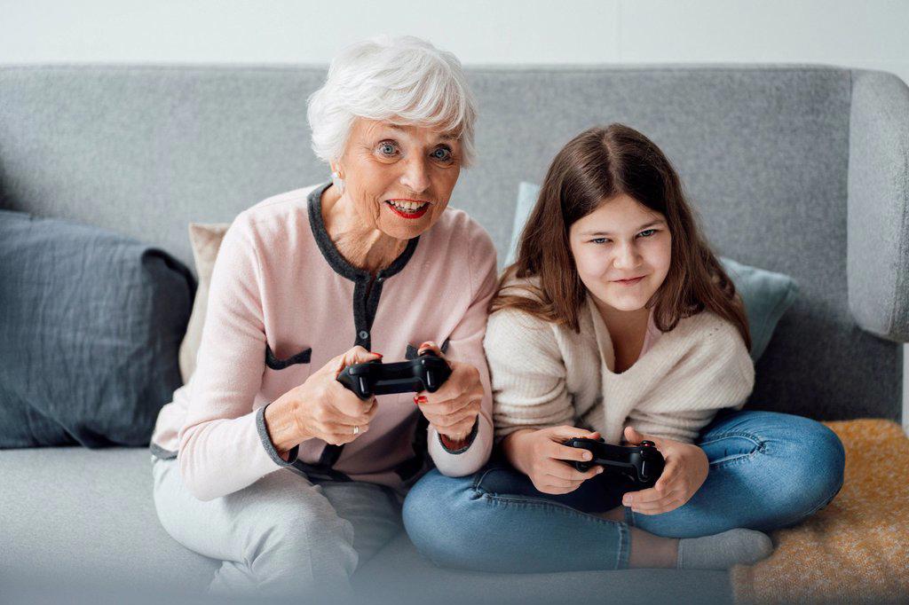 Grandmother playing video game with granddaughter at home