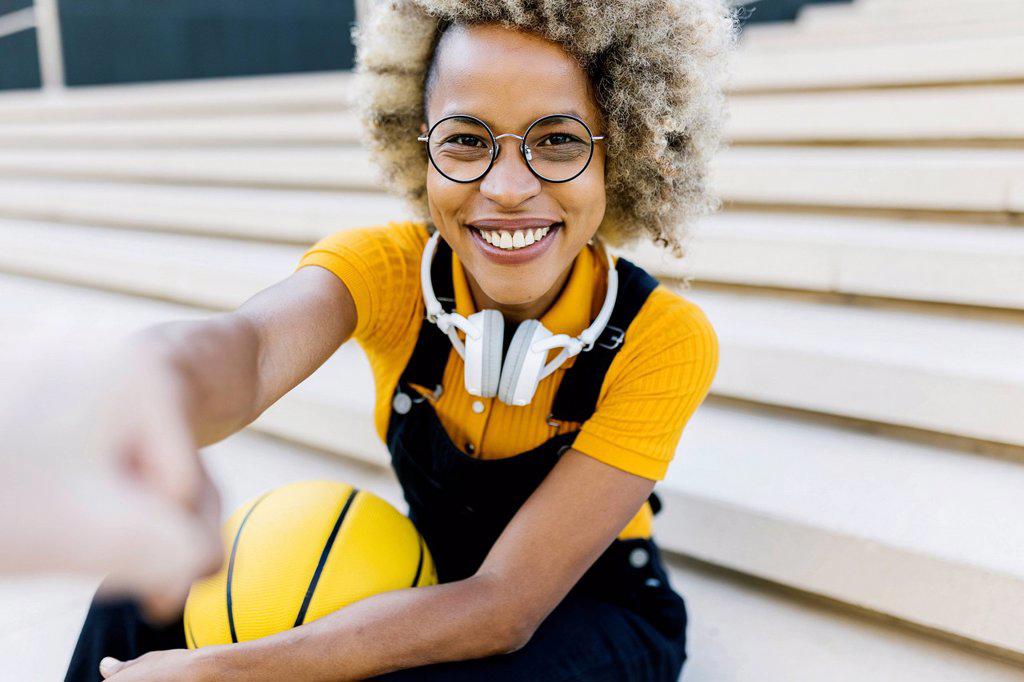 Smiling woman with headphones and eyeglasses on steps