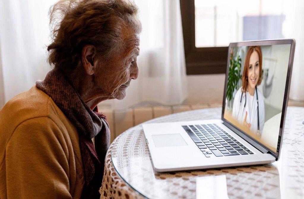 Doctor discussing with senior woman on video call through laptop at home