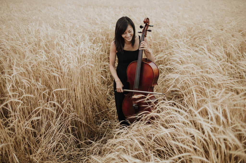 Smiling woman playing cello amidst crops in field