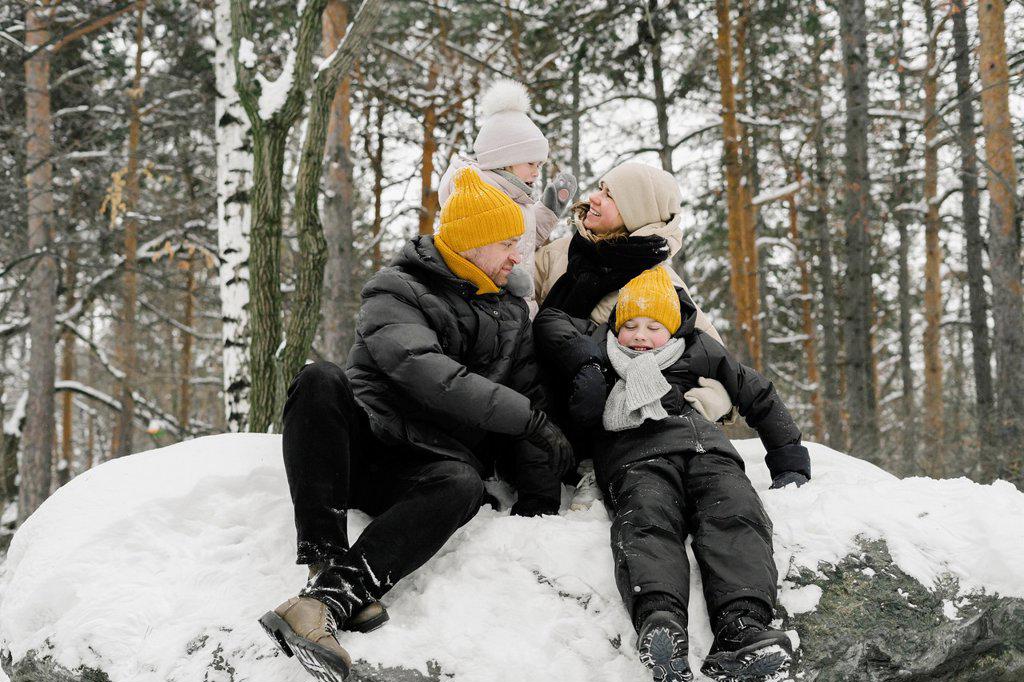 Man and woman sitting with daughter and son on snow in winter forest