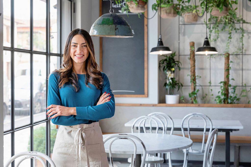 Smiling woman standing with arms crossed in cafe