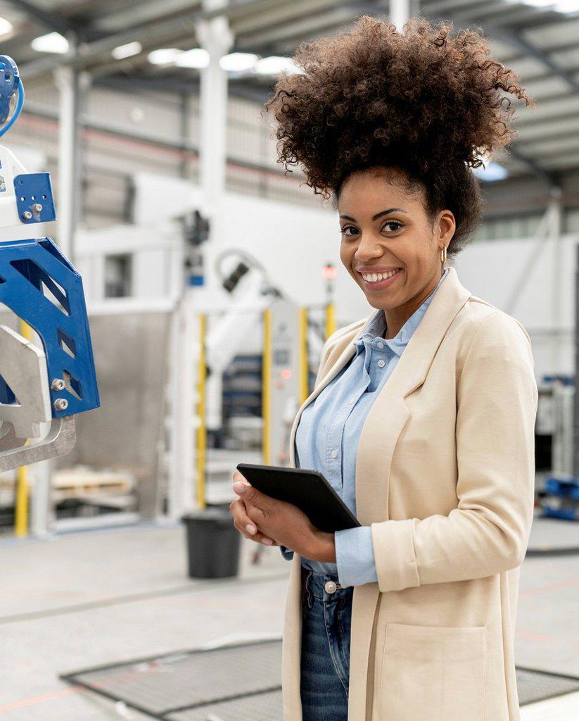 Happy businesswoman holding tablet PC standing in factory