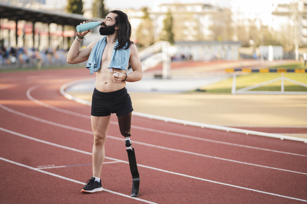 Athlete with prosthetic leg drinking water from bottle standing on running track