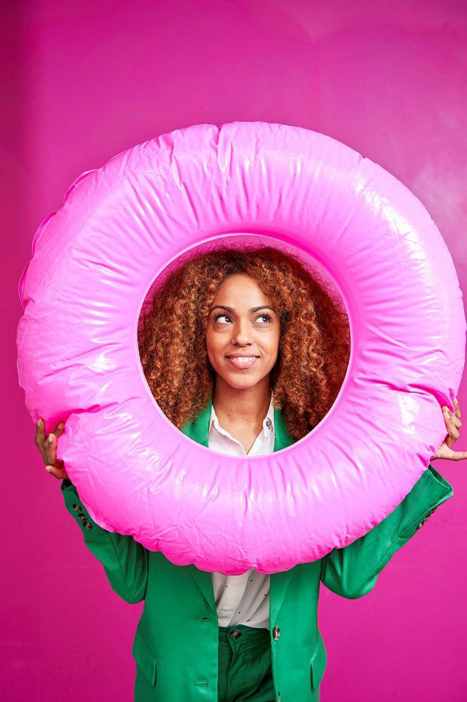Smiling businesswoman looking though inflatable ring against pink background