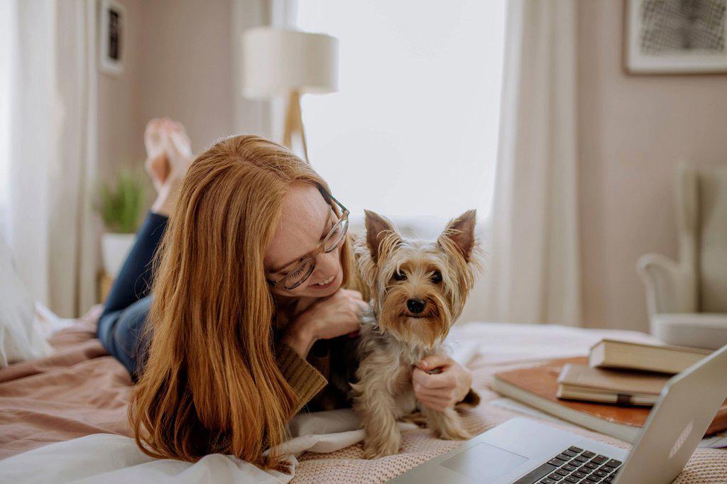 Smiling woman playing with pet dog lying on bed at home