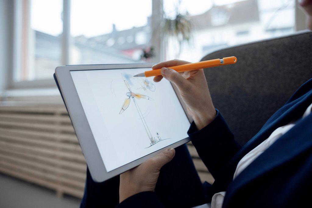 Hand of businesswoman drawing wind turbine on tablet PC in office