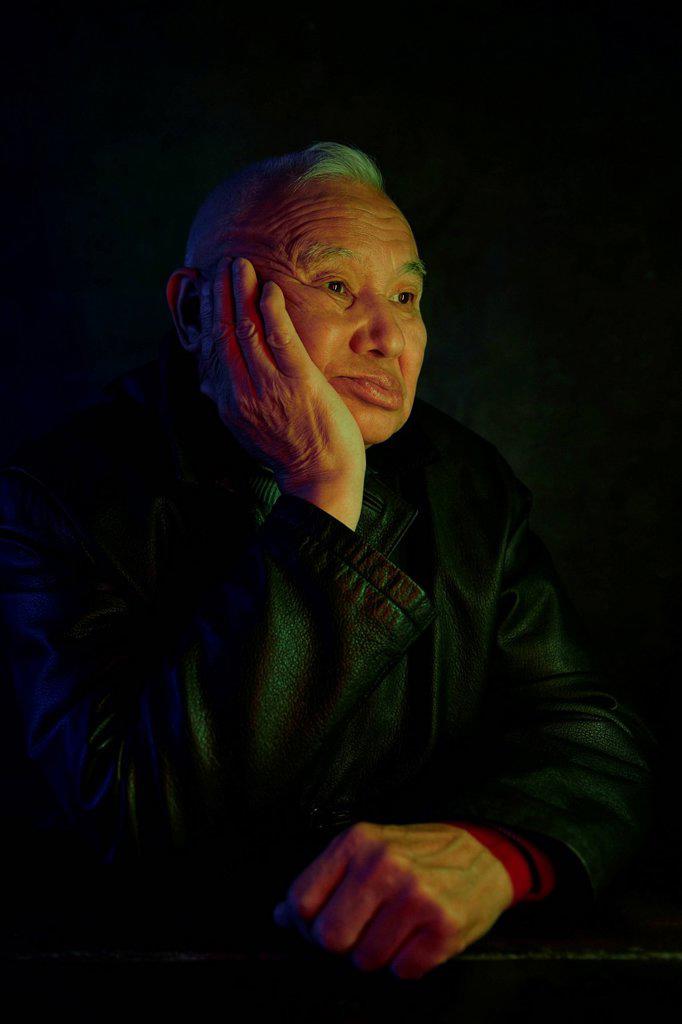 Pensive senior man sitting with hand on chin against black background