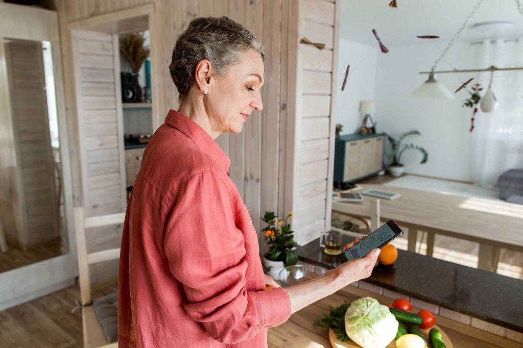 Woman in kitchen at home holding smartphone