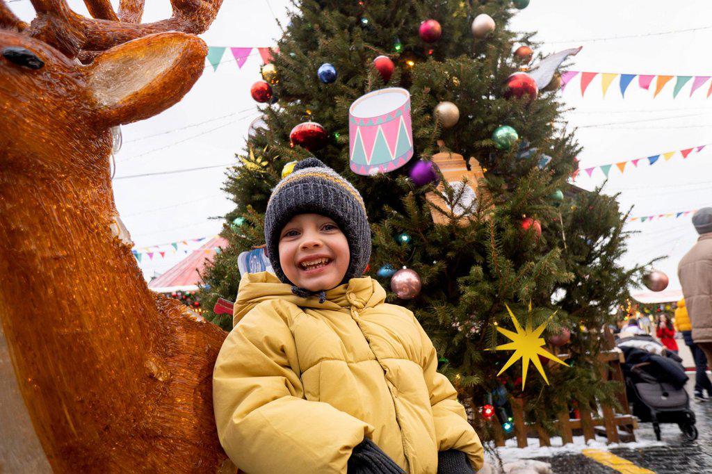 Happy boy standing by deer decoration at Christmas market