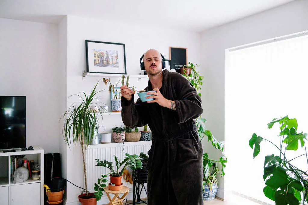 Carefree man with bowl enjoying music through wireless headphones at home