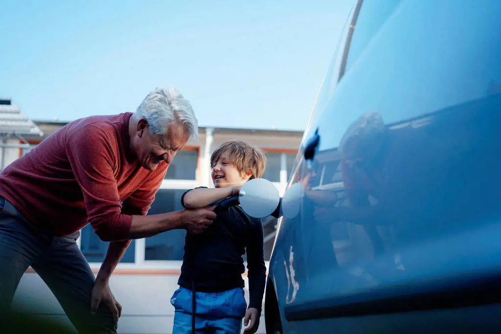 Happy senior man and grandson charging electric car