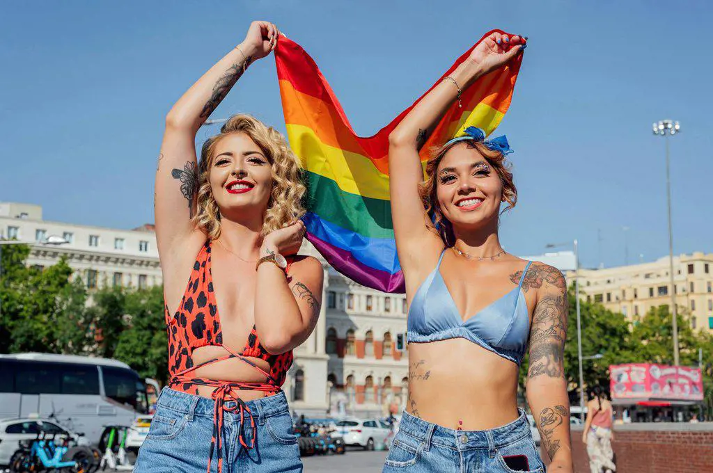 Happy women holding rainbow flag on sunny day