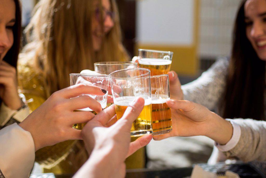 Friends toasting with beer glasses in a street cafe, close-up