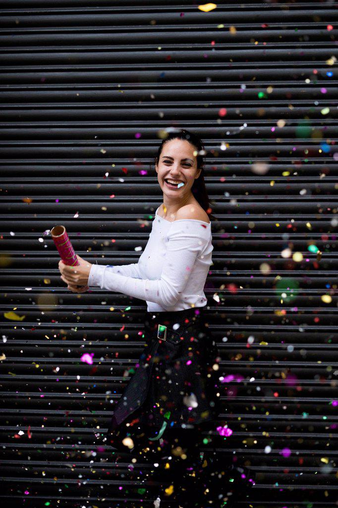 Happy young woman standing in front of black roller shutter throwing confetti