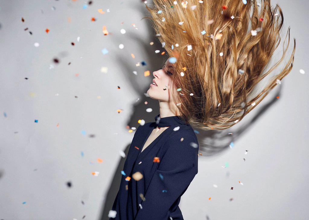 Young woman tossing hair under shower of confetti