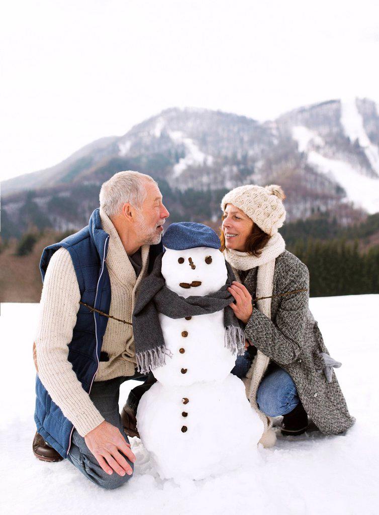 Senior couple with snowman in winter landscape