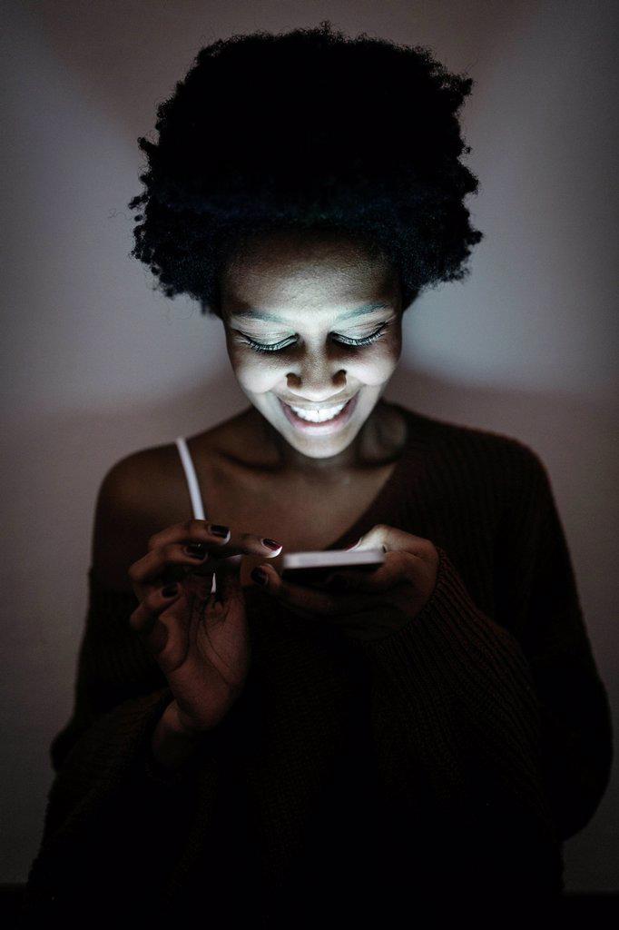 Smiling young woman using cell phone in the dark