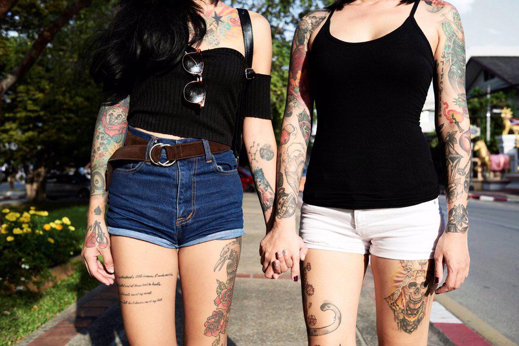 Tattooed lesbian couple holding hands in the street in summer