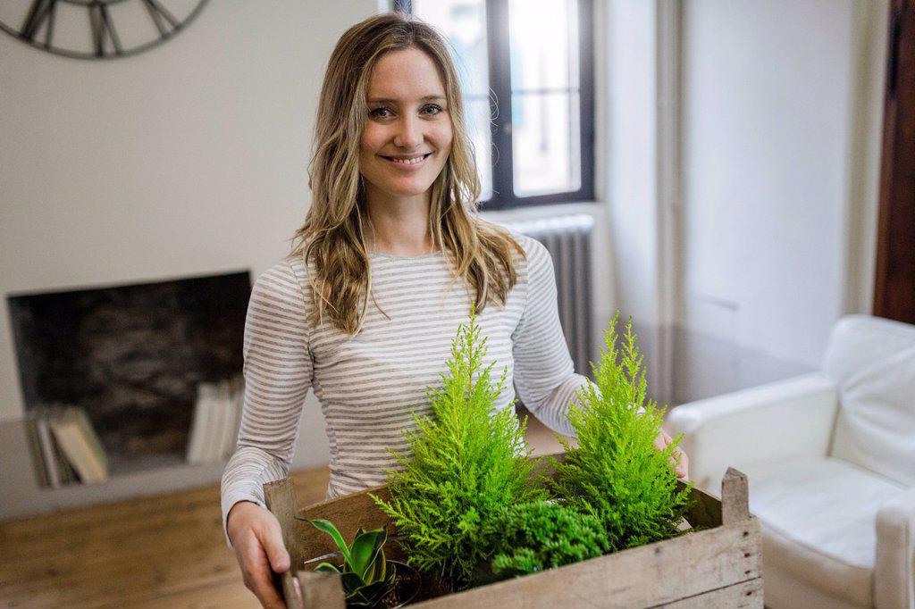 Portrait of smiling woman carrying crate with plants at home