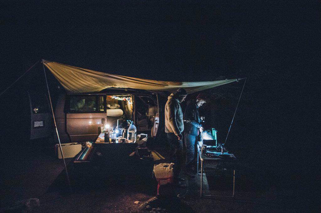 Canada, British Columbia, two men cooking under tarp at minivan at night