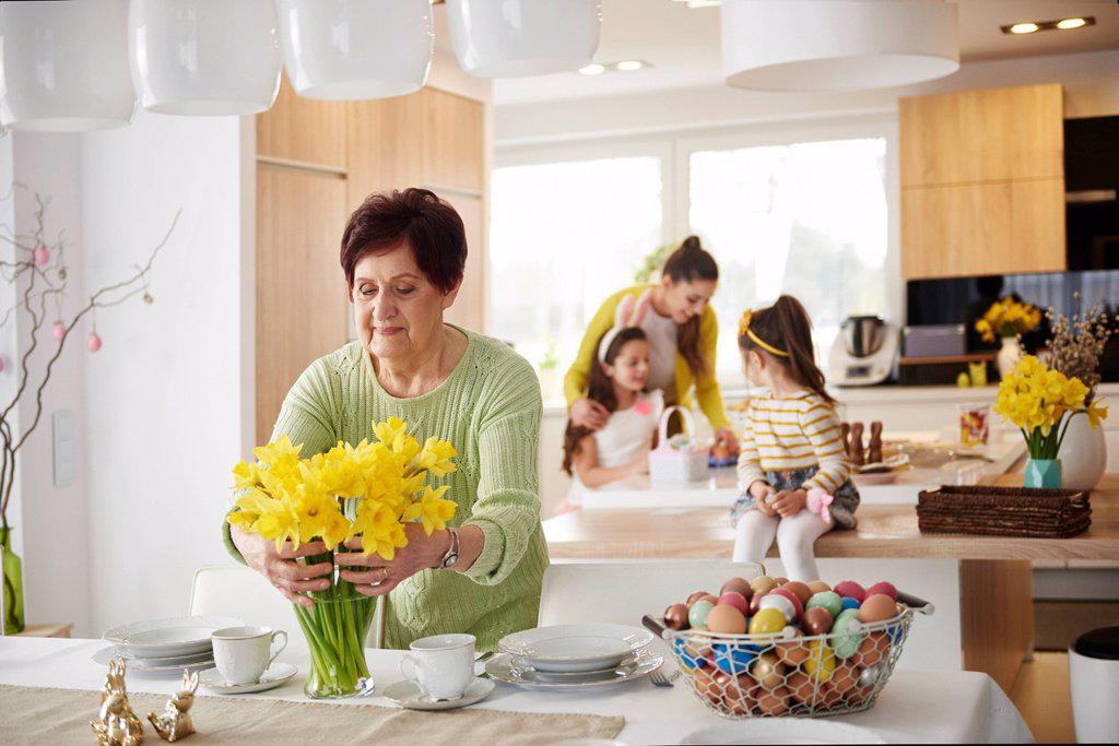Senior woman arranging flowers on dining table with family in background