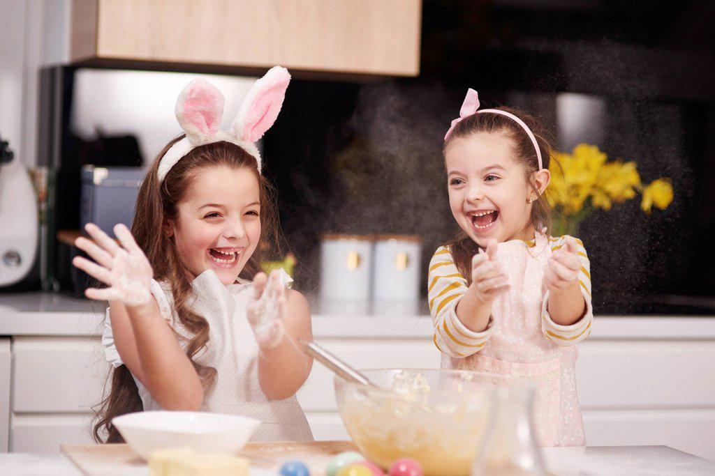 Two playful sisters having fun baking Easter cookies in kitchen together