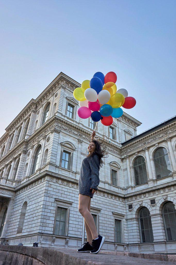 Germany, Munich, happy young woman with bunch of balloons