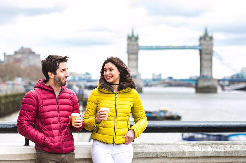 UK, London, couple with coffee to go standing on bridge over the Thames