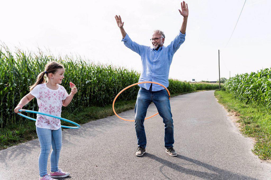 Grandfather and granddaughter playing with hoola hoop in the street