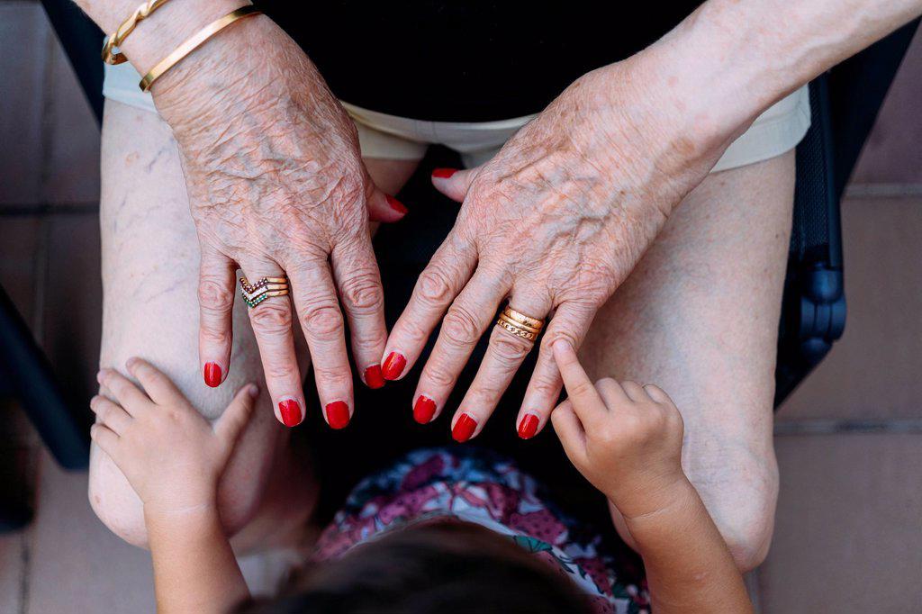 Hand of baby girl pointing on hand of senior woman with rings and red painted nails