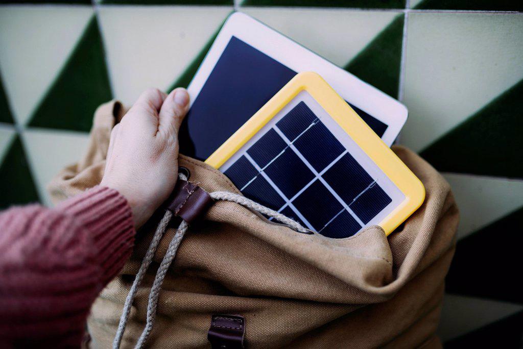 Woman putting a tablet into a backpack with a solar panel charger