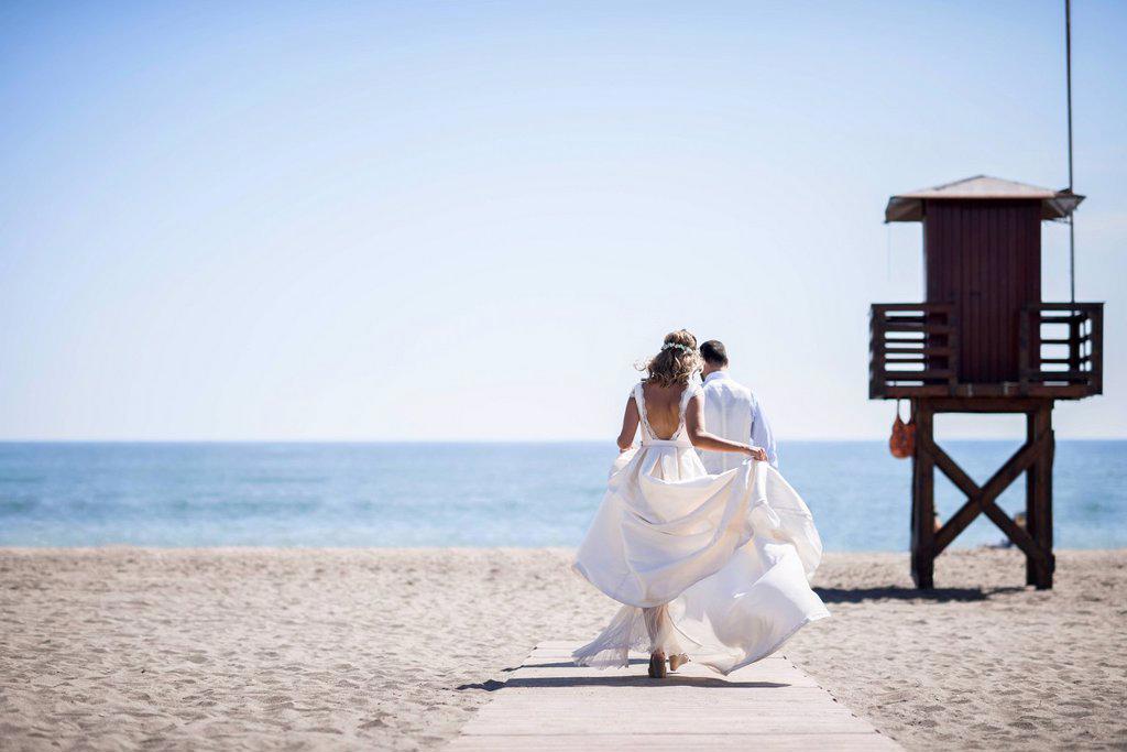 Back view of bridal couple enjoying wedding day walking on the beach