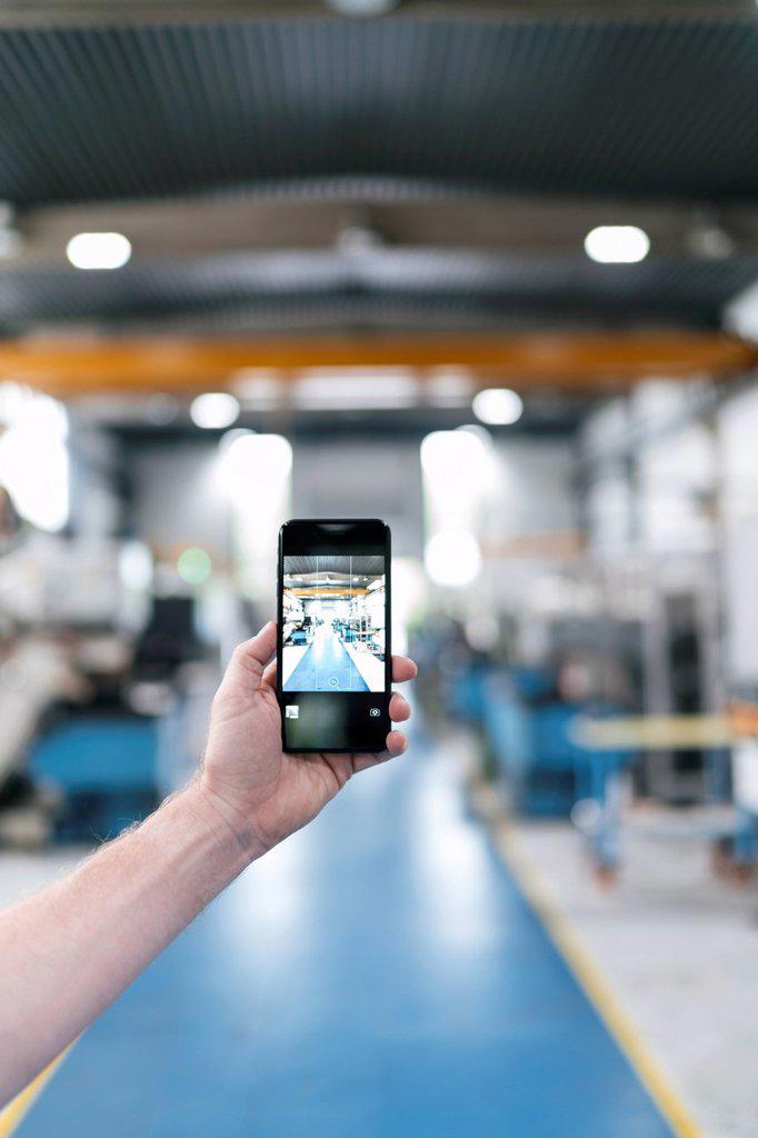 Hand holding smartphone in a factory workshop