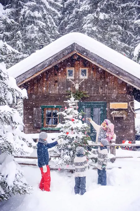 Austria, Altenmarkt-Zauchensee, family decorating Christmas tree at wooden house