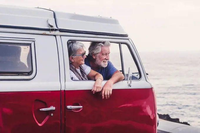 Senior couple traveling in a vintage van, looking at the sea