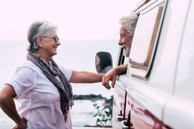 Senior couple traveling in a vintage van, taking a break at the sea, talking