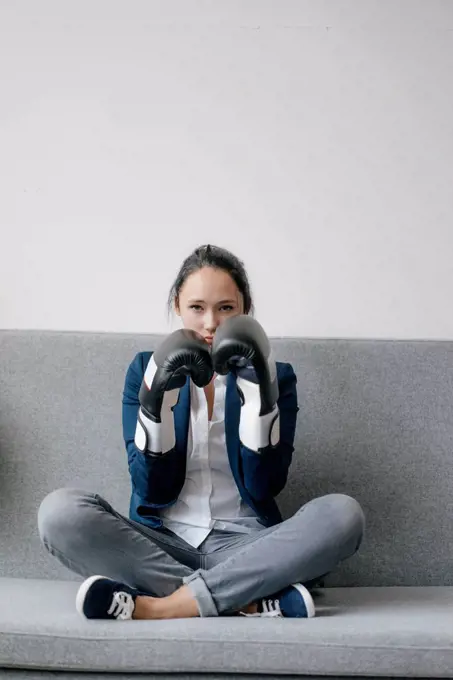 Portrait of young woman sitting on couch wearing boxing gloves
