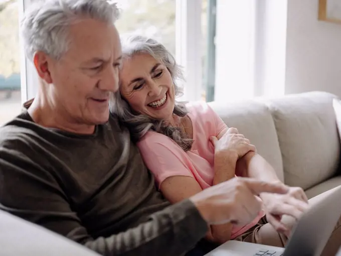 Happy senior couple with laptop relaxing on couch at home