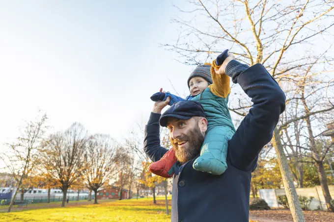 Happy man carrying his baby son on shoulders at park