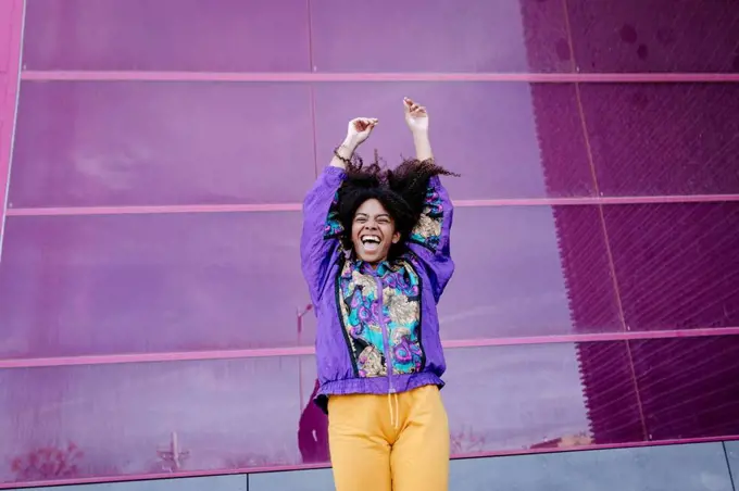 Young woman with urban look cheering in front of pink glass wall