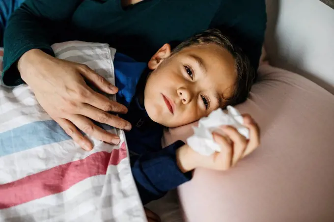 Portrait of sick little boy lying in bed